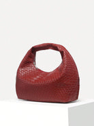 Rote Damenhandtasche aus Leder mit geflochtenem Muster auf weißem Podest.