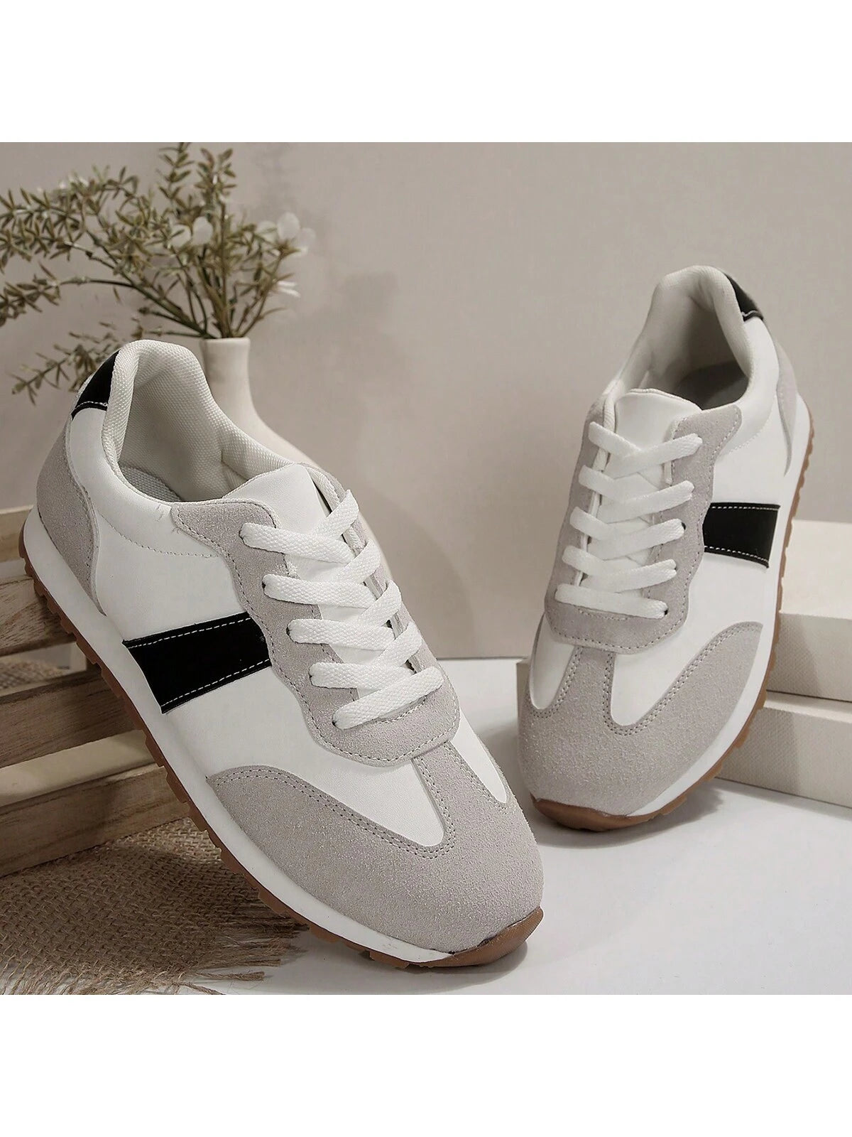 Weiße Sneaker mit grauen Akzenten, schwarzem Streifen, Gummisohle, auf Holzkiste, modern.