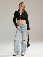 Frau in modischer Kleidung: Schwarzes Crop-Top-Blazer, zerrissene Jeans, weiße Sneaker. Trendige Damenmode, lässiger Streetstyle-Look.