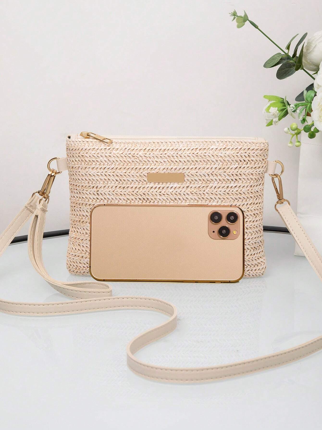 Beige Handtasche aus Stroh mit Smartphone, Blumen im Hintergrund, modisches Accessoire.