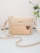 Beige Handtasche aus Stroh mit Smartphone, Blumen im Hintergrund, modisches Accessoire.