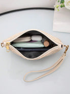 Beige Damenhandtasche aus Leder mit Reißverschluss, gefüllt mit Alltagsgegenständen, auf Tisch.