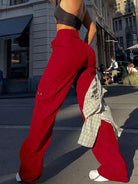Frau in roten Baggy-Hosen und schwarzem Top auf städtischer Straße. Modetrend, Streetwear, lässiger Stil, urbane Mode, Sommeroutfit.