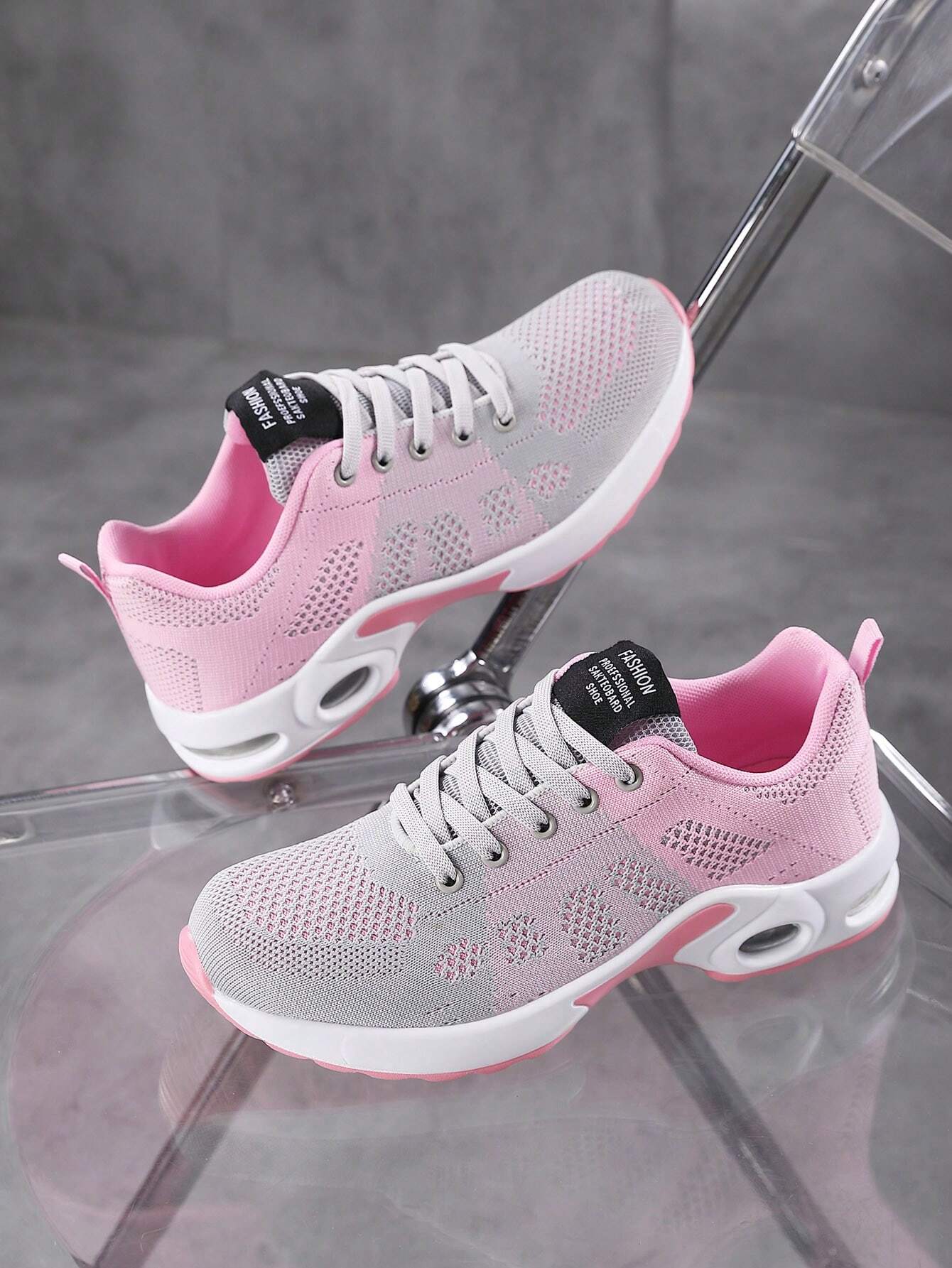 Graue und rosa Damen-Sneaker auf transparentem Stuhl, atmungsaktiv, sportlich, modisch.