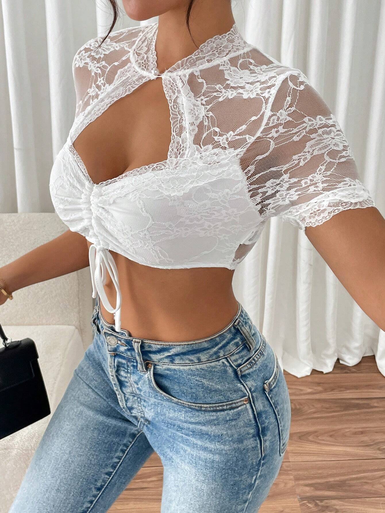 Damenmode: Weißes Spitzen-Crop-Top mit Schnürung, kombiniert mit blauen Jeans. Elegantes Design, ideal für trendige Sommer-Outfits.