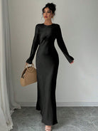 Elegantes schwarzes Maxikleid mit langen Ärmeln, kombiniert mit einer stilvollen, runden Strohtasche. Perfekt für Abendmode und besondere Anlässe.