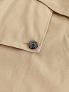 Beige Trenchcoat-Detail mit schwarzem Knopf, hochwertiger Stoff, klassisches Design, ideal für stilvolle Herbst- und Wintermode.