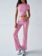 Frau in rosa Sportbekleidung: enges Crop-Top und weite Jogginghose, kombiniert mit weißen Sneakers. Perfekt für Fitness und Freizeit.