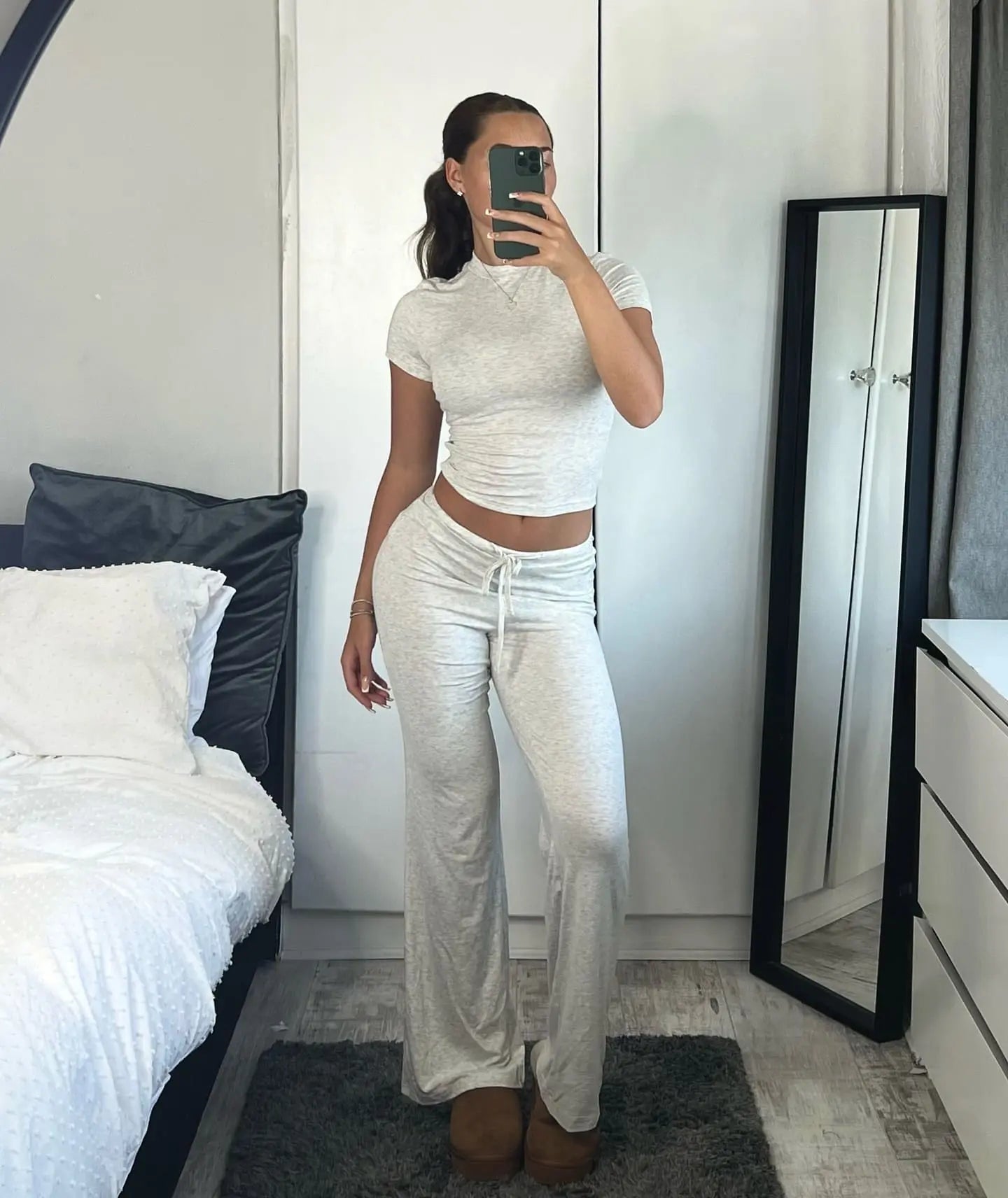 Frau in grauem Lounge-Set posiert vor Spiegel, gemütliche Mode, Homewear, bequeme Kleidung, modernes Schlafzimmer, Selfie, Freizeitlook.