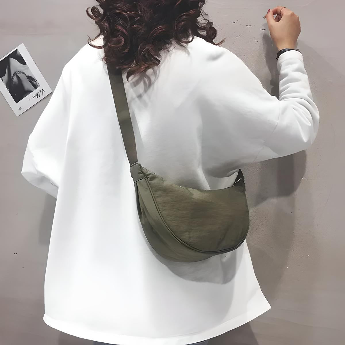 Frau mit weißem Pullover und olivgrüner Umhängetasche aus Stoff, Rückansicht.