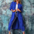 Frau trägt blauen Strickmantel mit Pompons, kombiniert mit Jeans und weißem Top. Modetrend, Damenmode, Herbstoutfit, Strickmode.