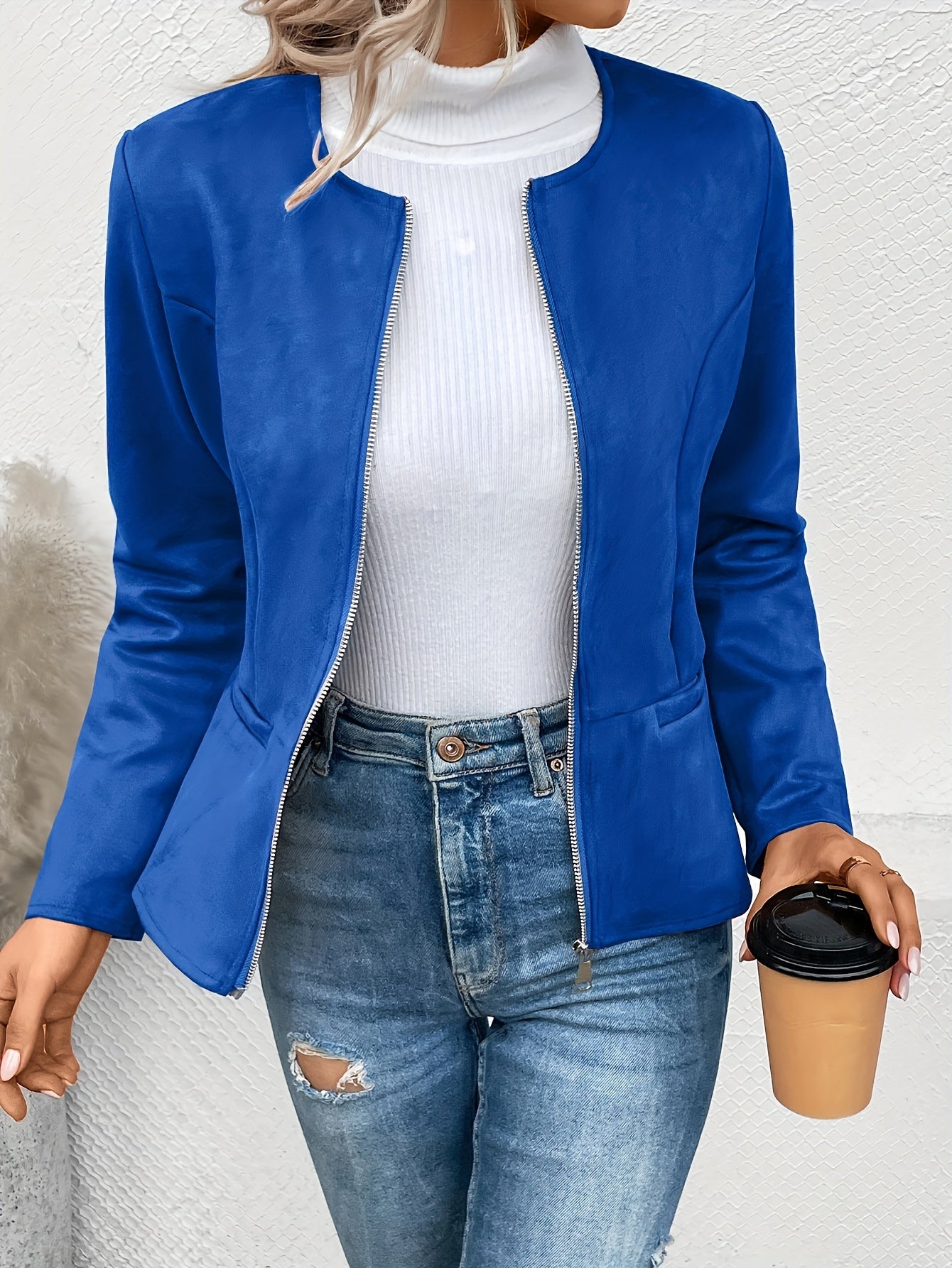 Frau in blauer Jacke, weißem Rollkragenpullover und Jeans hält Kaffeebecher. Modetrend, Damenmode, Freizeitlook, stilvolle Kleidung.
