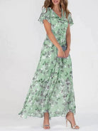 Frau in langem, grünem Blumenkleid, Sommermode, elegante Damenbekleidung, fließender Stoff.