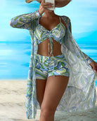 Frau in stilvollem, gemustertem Strandoutfit mit Bikini und passendem Kimono vor tropischem Hintergrund. Perfekt für Sommermode und Strandurlaub.