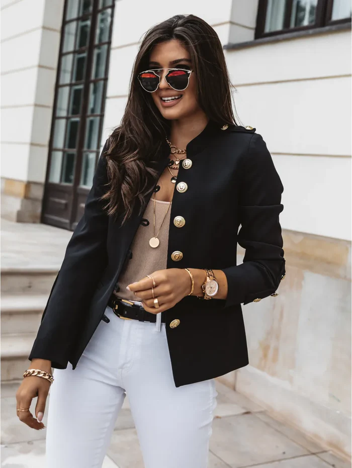 Elegante Frau in schwarzer Jacke mit goldenen Knöpfen, weißer Hose und Sonnenbrille. Modetrend, stilvolle Damenmode, urbaner Chic.