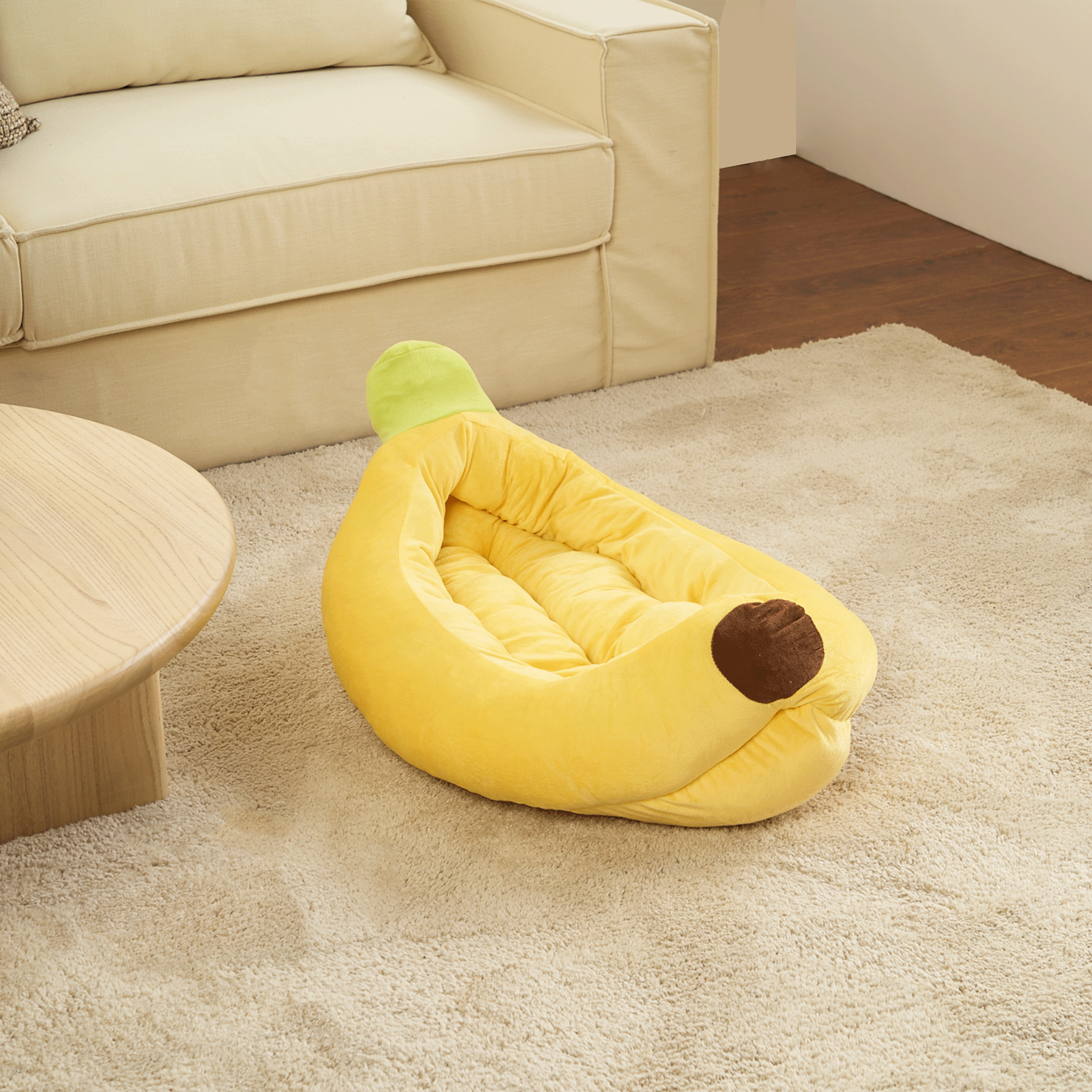 Gelbes Bananen-Split-Haustierbett aus Plüsch auf beigem Teppich neben Sofa und Holztisch.