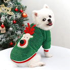 Weißer Hund in grünem Rentier-Pullover vor Weihnachtsbaum. Niedliches Haustier, Weihnachtsoutfit, festliche Hundebekleidung, Wintermode.