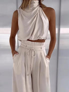 Elegantes Damen-Outfit: Weißes, ärmelloses Oberteil mit Drapierung und hoch taillierte Hose. Perfekt für stilvolle Anlässe und moderne Mode.