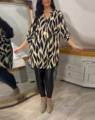 Damenmode: Langes, schwarz-weiß gemustertes Hemd, kombiniert mit schwarzer Leggings und beigen Stiefeletten. Perfekt für stilvolle Freizeitlooks.