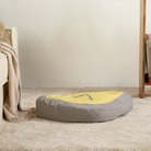 Graues und gelbes Haustierbett aus Plüsch, rund, auf Teppichboden im Wohnzimmer.