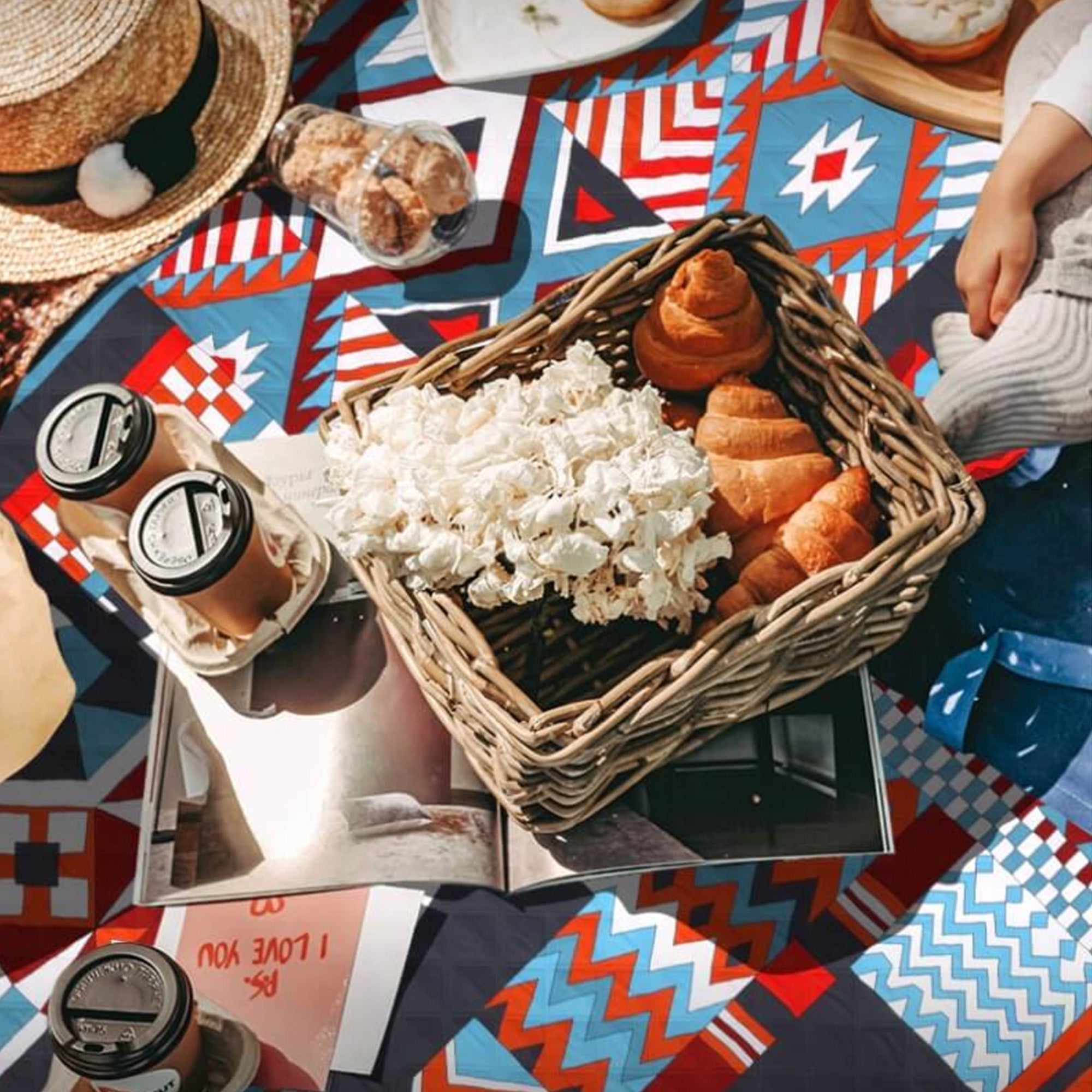 Bunte Picknickdecke mit Korb voller Croissants und Popcorn, ideal für Outdoor-Aktivitäten.