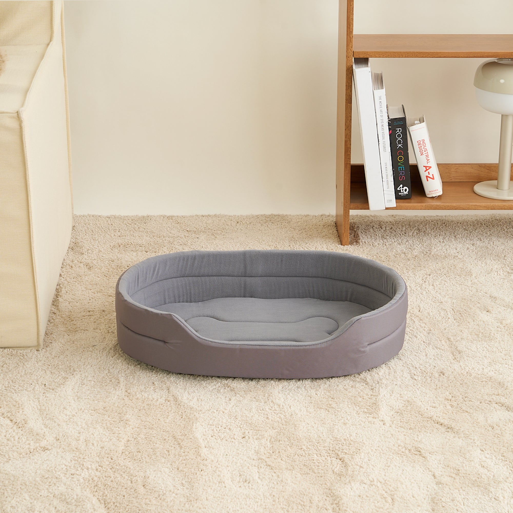 Graues Hundebett aus Stoff auf Teppich, oval, gemütlich, ideal für kleine Haustiere.