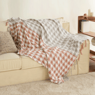 Beige Sofa mit Hahnentritt-Decke in Grau und Rostrot, Quasten, Wohnzimmer-Dekoration.