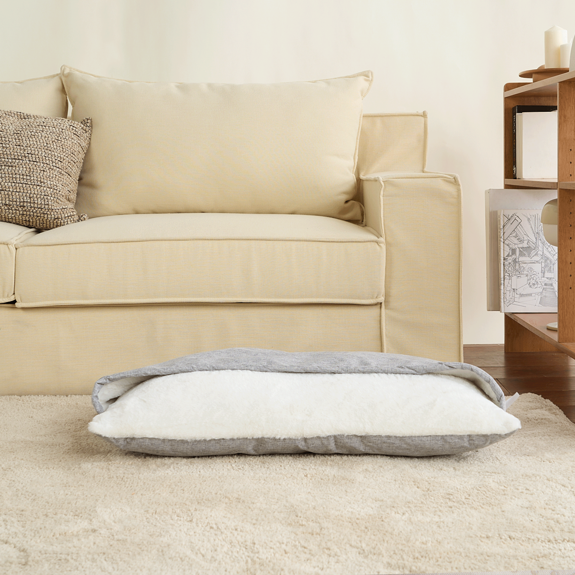 Ultraweicher Haustier-Schlafsack in Grau und Weiß auf Teppich vor beigem Sofa im Wohnzimmer.