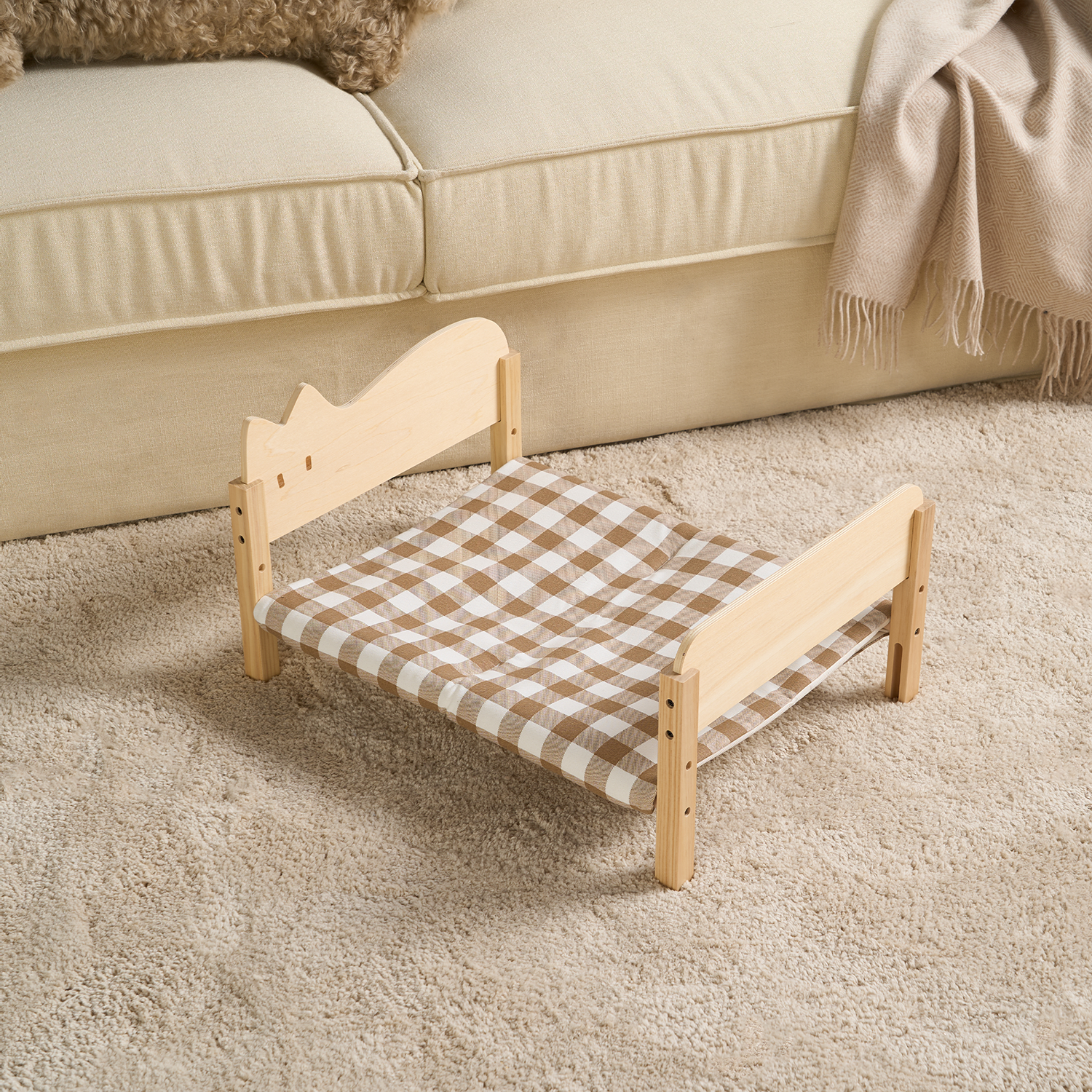 Holzbett für Katzen mit kariertem Stoff, modernes Design, auf beigem Teppich vor Sofa.