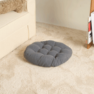 Graues, rundes Tatami-Kissen auf beigem Teppich neben Sofa, ideal für Meditation und Entspannung.