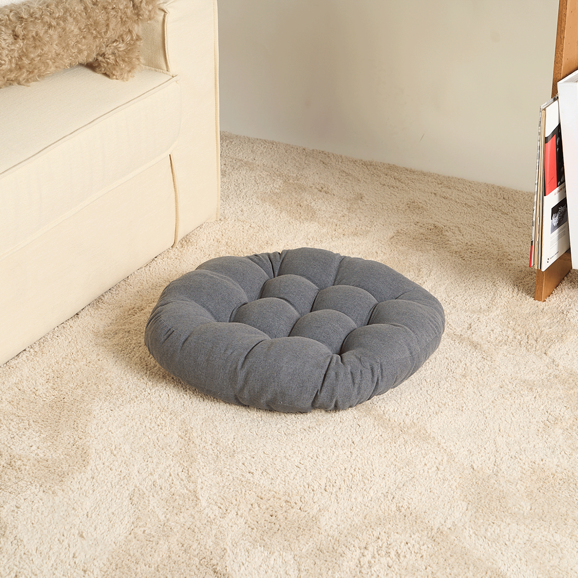 Graues, rundes Tatami-Kissen auf beigem Teppich neben Sofa, ideal für Meditation und Entspannung.