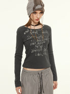 Damenmode: Graues Langarmshirt mit abstraktem Print, kombiniert mit grauer Hose und Mütze. Trendige Streetwear für Herbst/Winter.