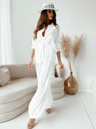 Elegantes weißes Sommeroutfit für Damen, bestehend aus lockerer Bluse und Hose, kombiniert mit Sonnenhut und Sandalen. Perfekt für stilvolle Anlässe.
