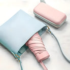 Hellblauer Ledertasche mit rosa Regenschirm und Etui auf weißem Hintergrund.