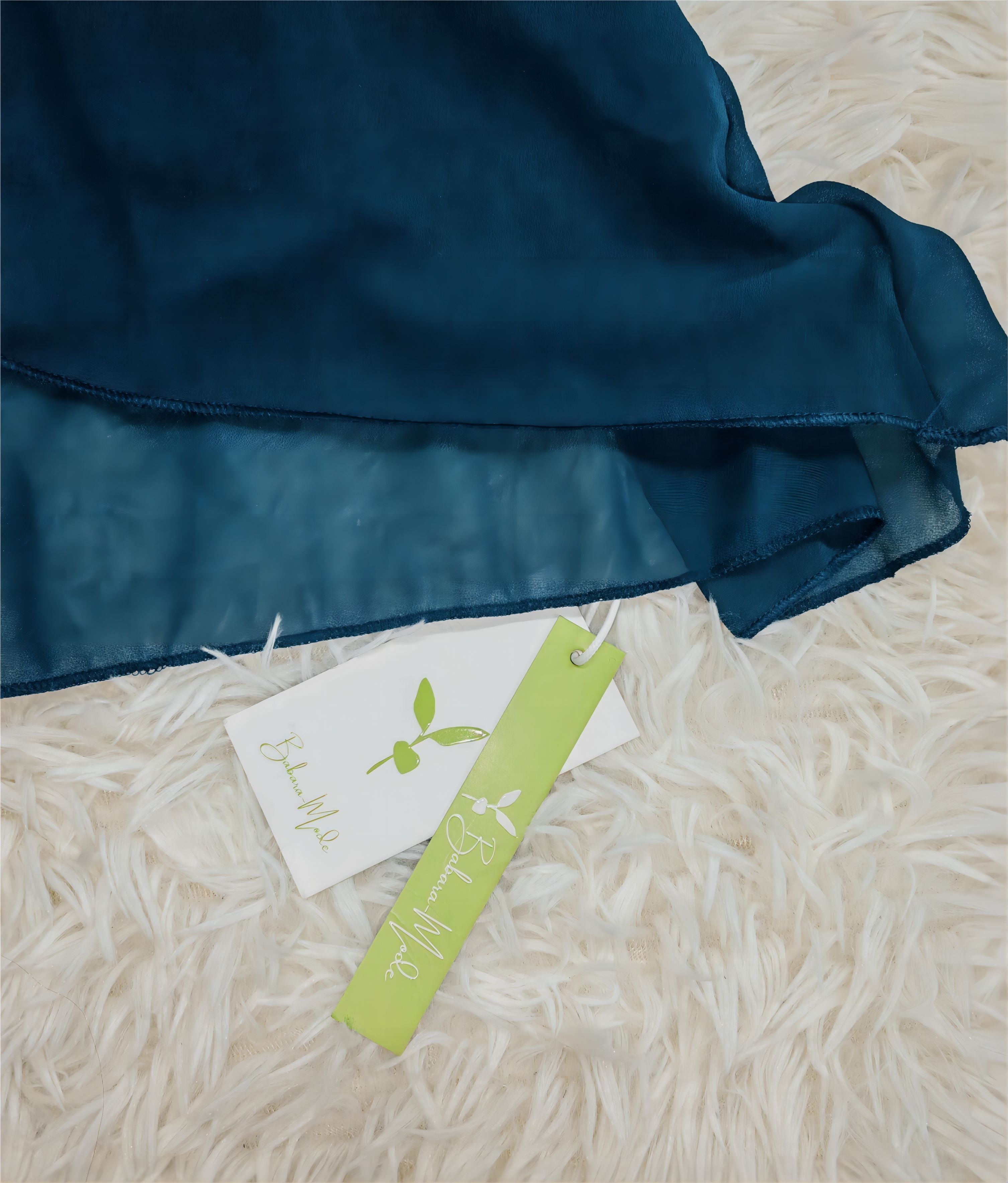 Dunkelblaues Seidenkleid auf weißem Teppich, mit grünen und weißen Etiketten. Hochwertige Mode, elegante Damenbekleidung, luxuriöse Stoffe.