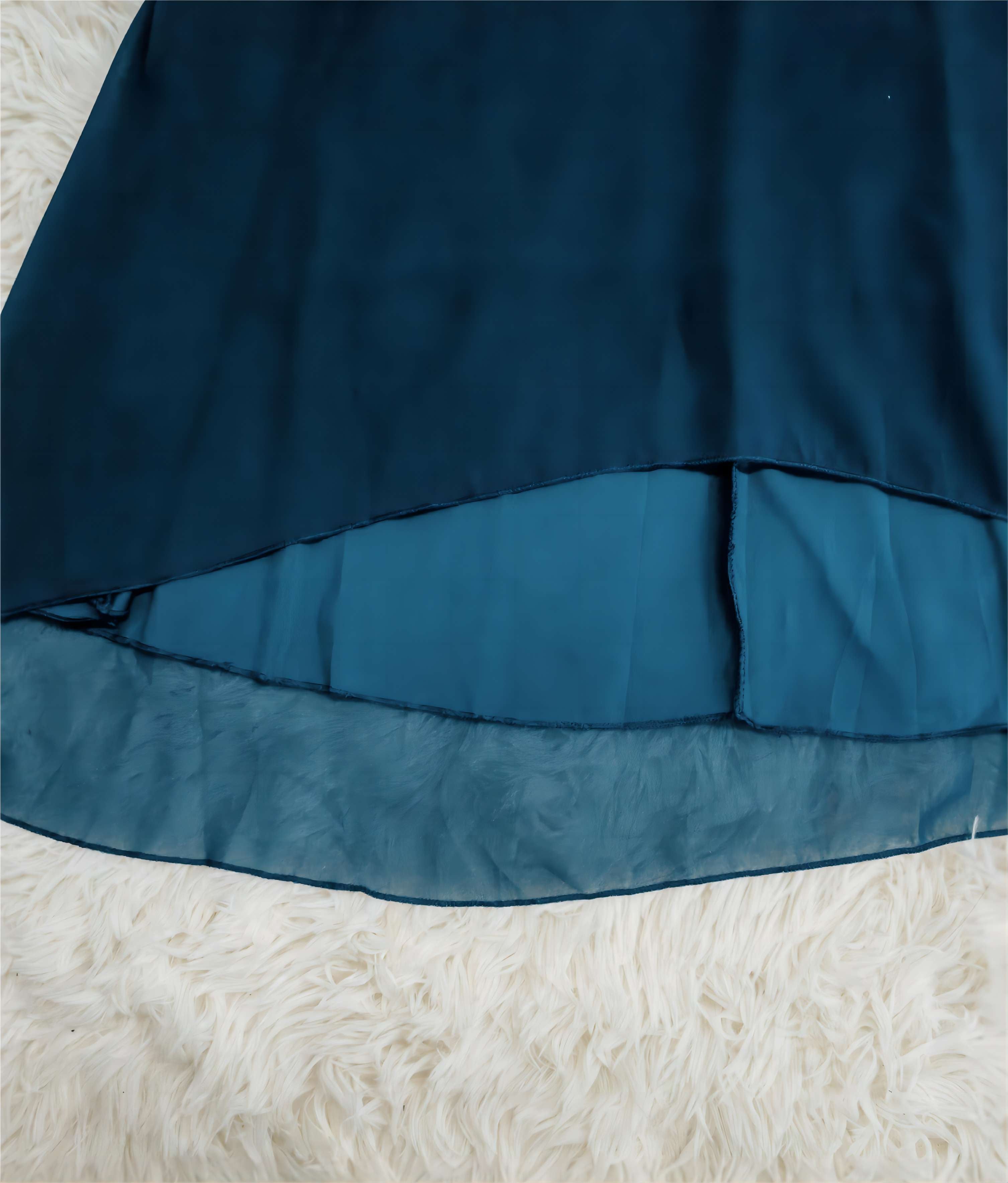 Elegantes, blaues Satinkleid mit asymmetrischem Saum auf weichem, cremefarbenem Teppich. Perfekt für Abendveranstaltungen und besondere Anlässe.