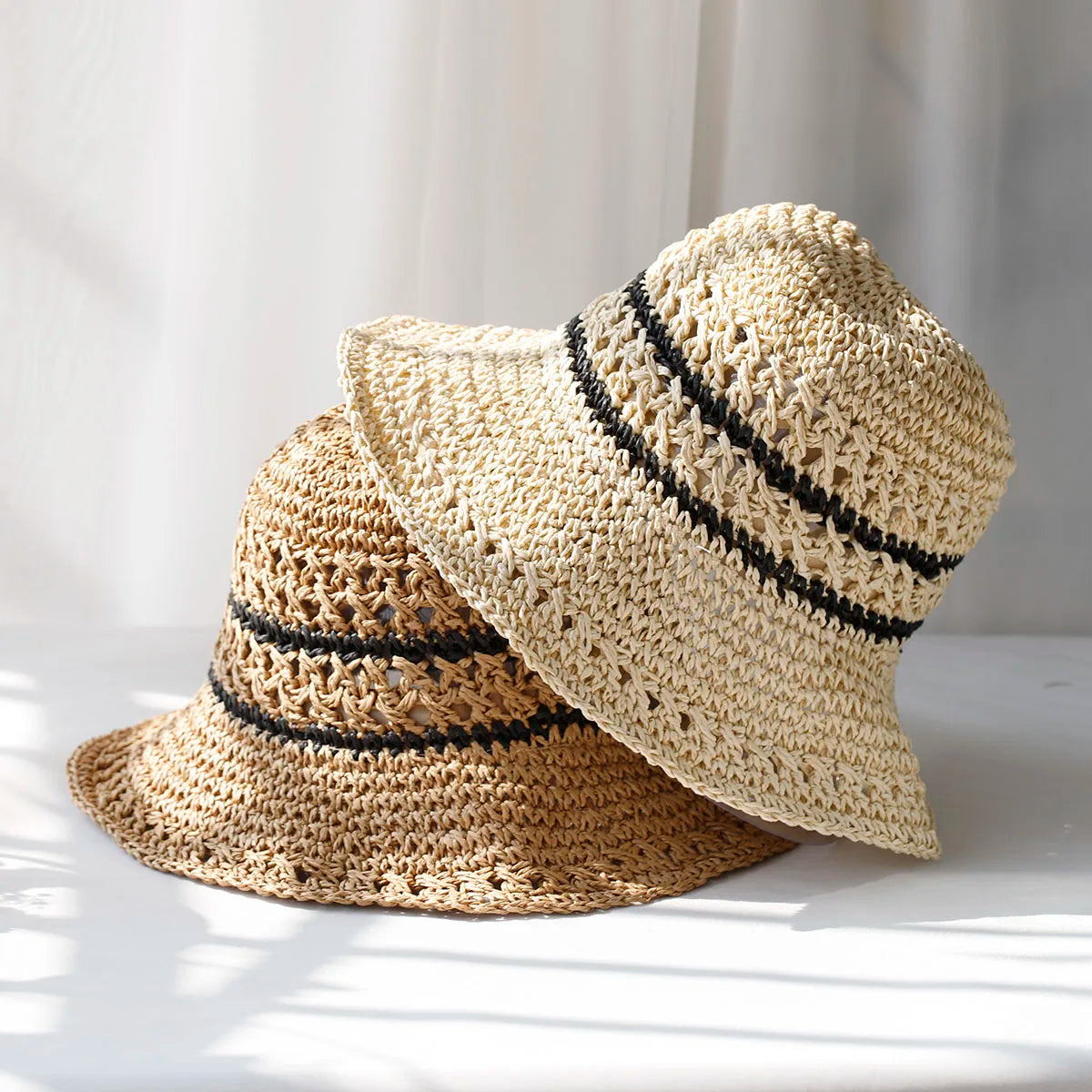 Zwei gehäkelte Damenstrohhüte mit UV-Schutz, gestreiftem Design und Fischerhut-Stil. Perfekt für Sommermode und Sonnenschutz.