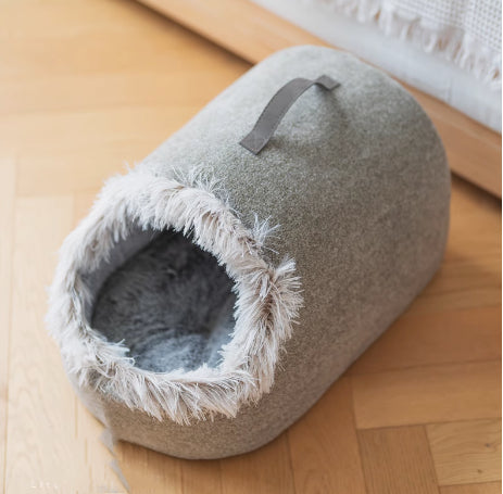 Graues Katzenbett aus Filz mit Plüschrand, gemütlich, modern, für Haustiere, auf Holzboden.