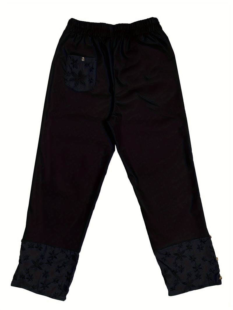Schwarze Jogginghose mit elastischem Bund, floralem Muster und aufgesetzter Tasche. Bequeme Freizeithose für Damen und Herren.