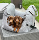 Zwei braune Dackel auf grauem Hundebett im Freien, gemütlich und entspannt.