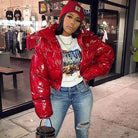 Frau in roter Daunenjacke, Jeans und Mütze posiert vor einem Geschäft. Modetrend, Streetwear, Wintermode, urbaner Stil, lässiger Look.