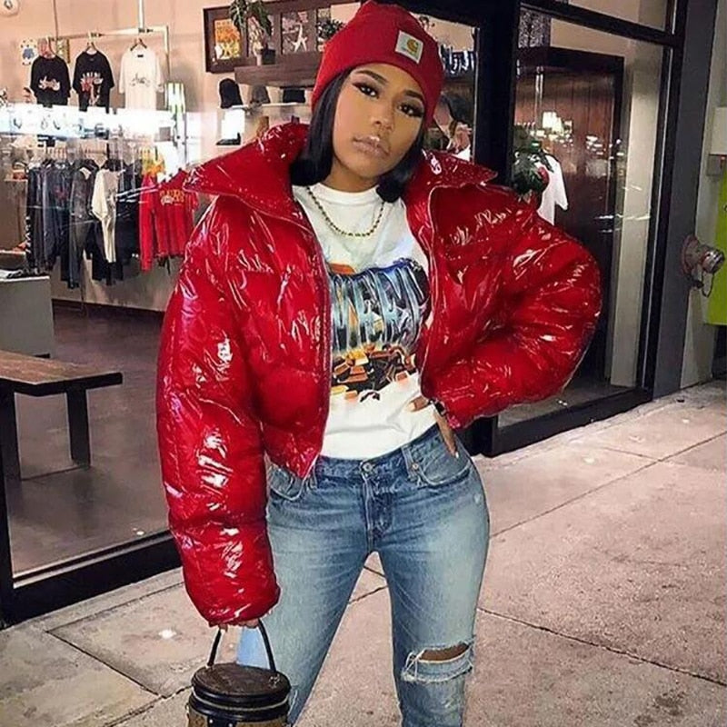 Frau in roter Daunenjacke, Jeans und Mütze posiert vor einem Geschäft. Modetrend, Streetwear, Wintermode, urbaner Stil, lässiger Look.