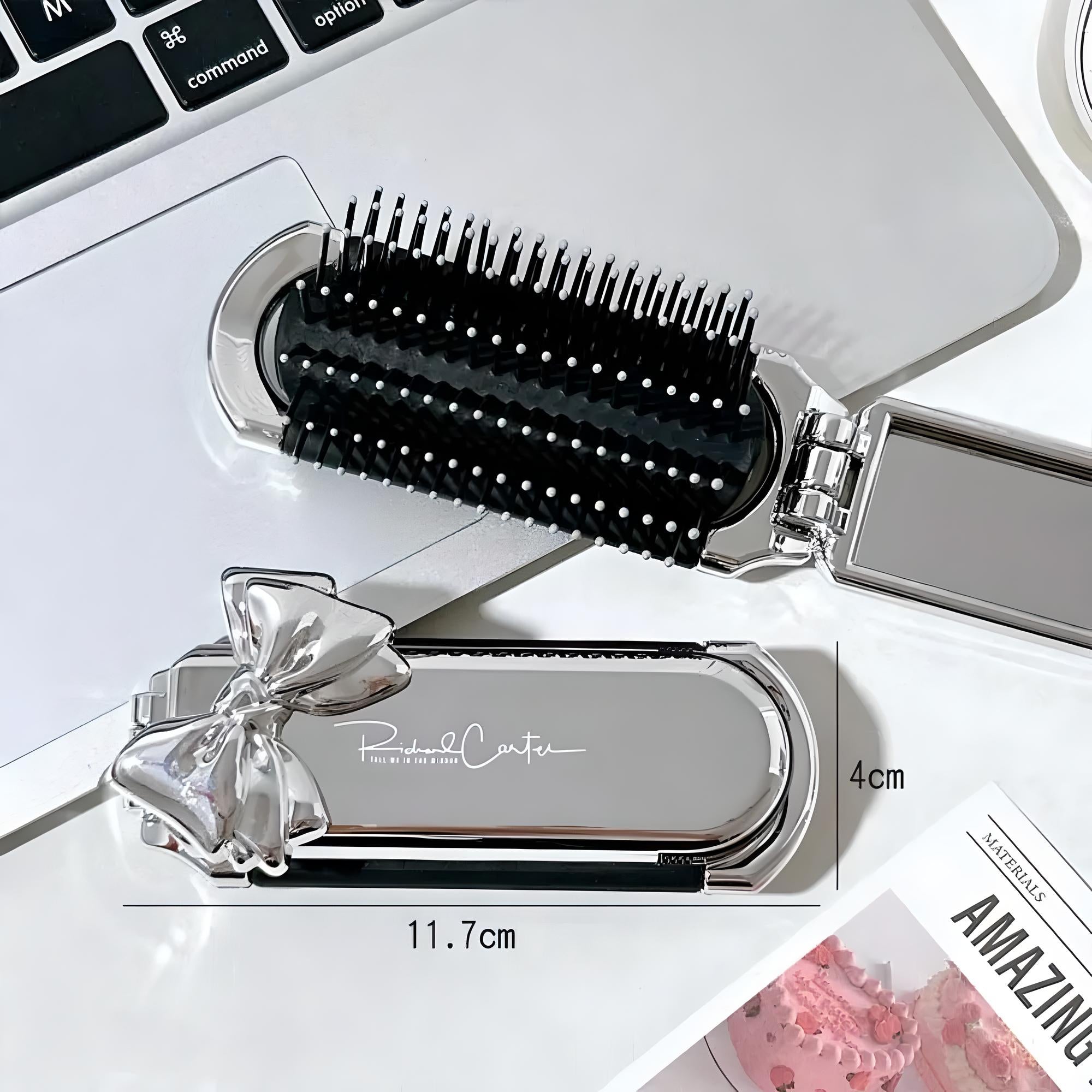 Silberne Haarbürste mit Schleife, kompakt, 11,7 cm, neben Laptop und Magazin auf Tisch.