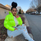 Frau in neongrüner Jacke und zerrissenen Jeans sitzt auf Bordstein; modischer Streetstyle, Wintermode, trendige Damenbekleidung, urbaner Look.