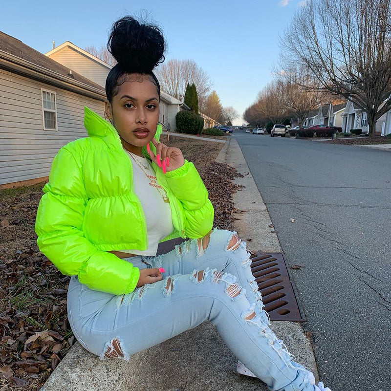 Frau in neongrüner Jacke und zerrissenen Jeans sitzt auf Bordstein; modischer Streetstyle, Wintermode, trendige Damenbekleidung, urbaner Look.