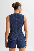 Frau in ärmellosem, tailliertem Jeans-Top und Shorts, Rückansicht. Modetrend, Denim, Sommeroutfit, lässiger Stil, Damenbekleidung.