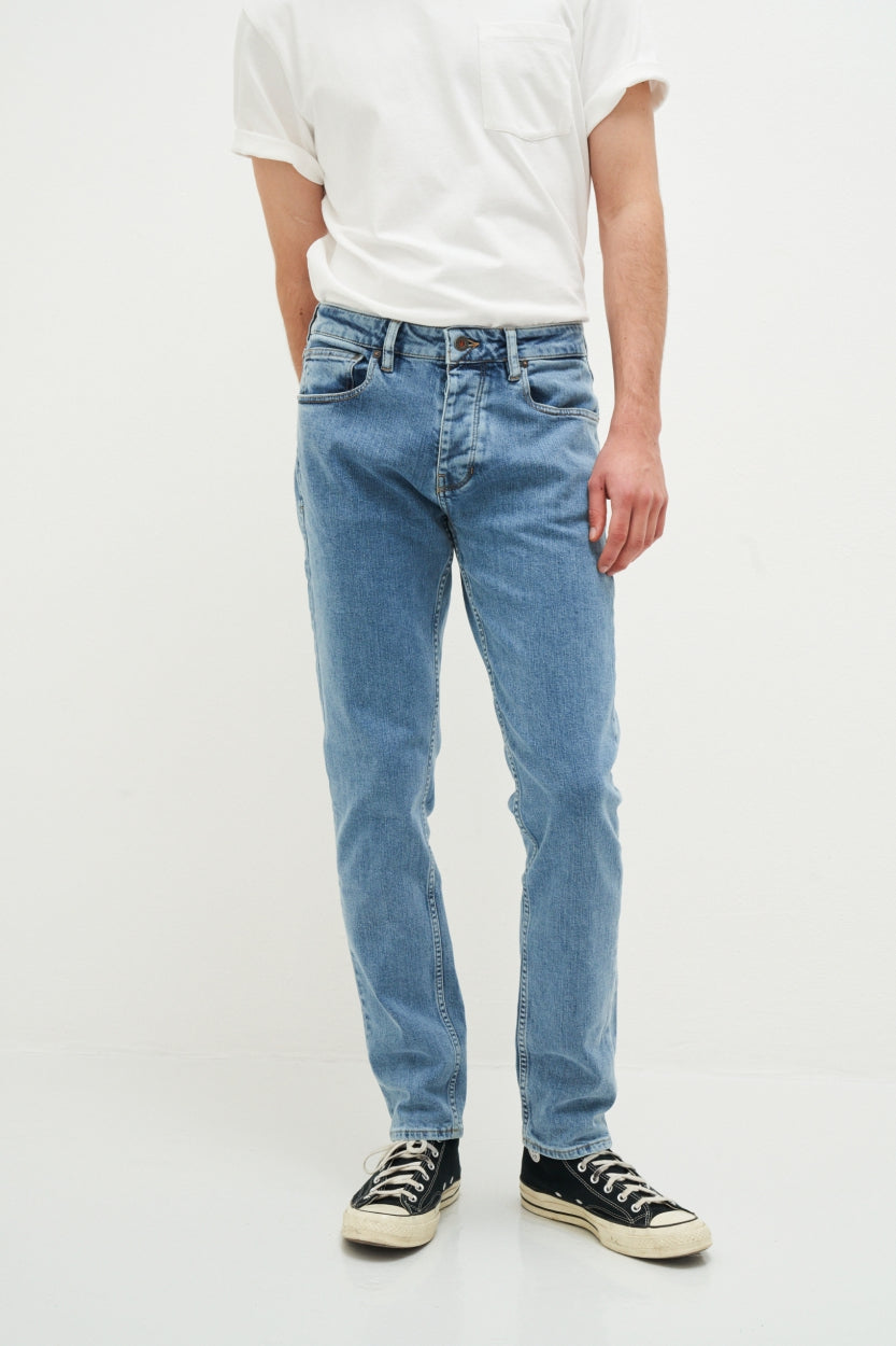 Mann in blauer Vintage-Jeans und weißem T-Shirt, schwarze Sneaker, lässiger Look.