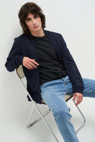 Mann in blauer Bomberjacke und Jeans auf Stuhl, lässige Mode, Herrenbekleidung, Freizeitlook.