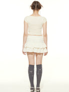 Frau in weißem Top und Rock, graue Kniestrümpfe, Rückansicht. Modetrend, Sommeroutfit, Damenbekleidung, stilvoll, lässig, modern.