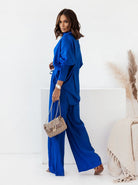 Frau in elegantem, blauem Jumpsuit mit modischer Handtasche. Perfektes Outfit für stilvolle Anlässe. Damenmode, Trend, Fashion, Stil.